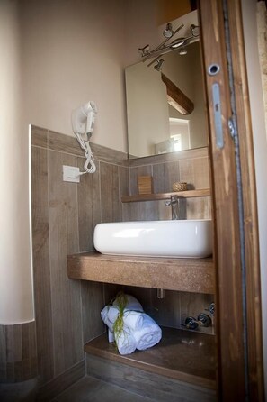 Un baño con un lavabo blanco, estantes de madera, un perchero para toallas y un espejo.
