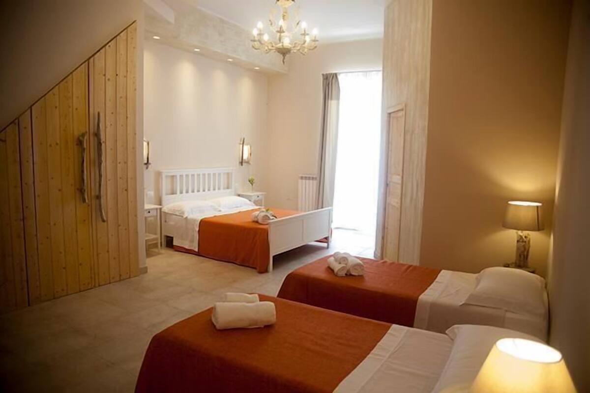 Una habitación de hotel con dos camas, un armario de madera, una araña y una ventana con cortinas.