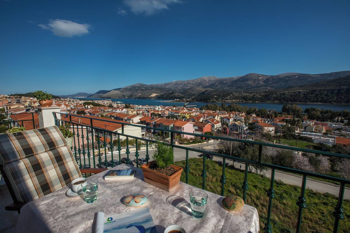 Een balkon met een tafel voor twee, met uitzicht op een stad en een meer.