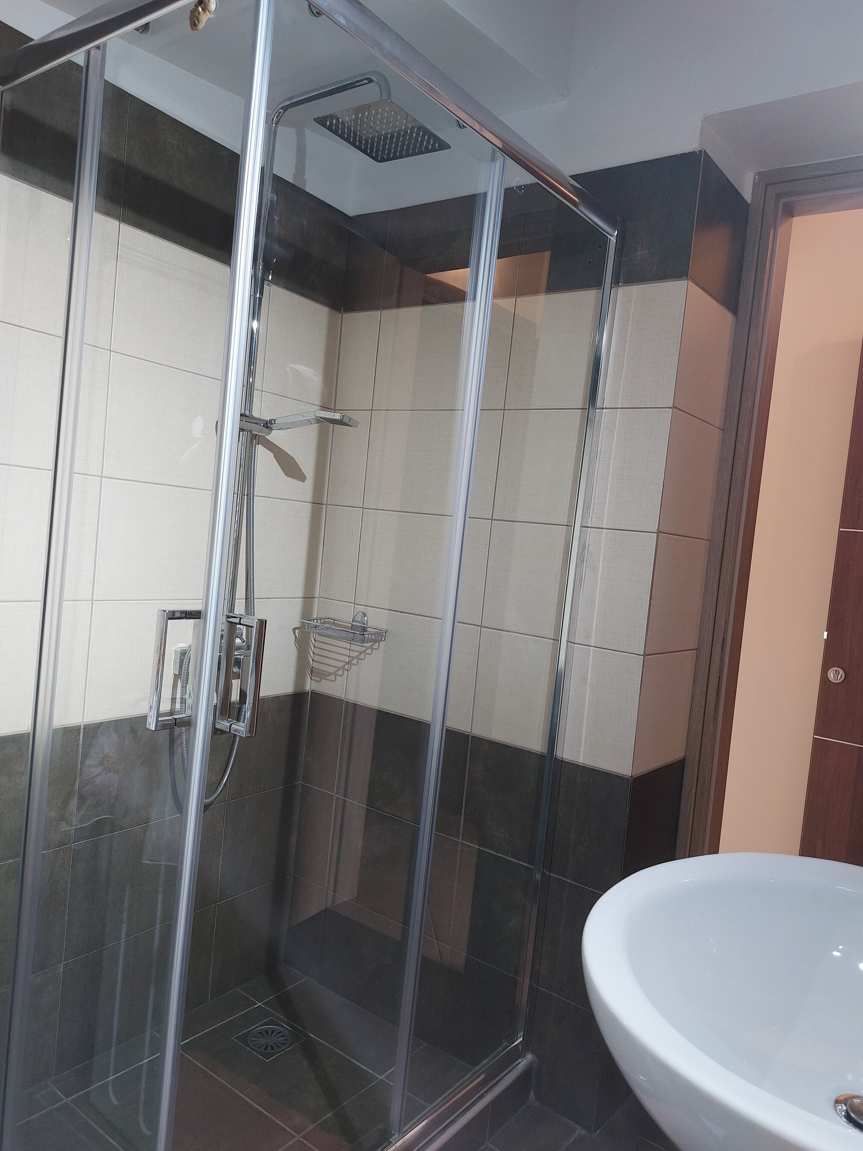 A glass-enclosed shower with a handheld showerhead and a wall-mounted faucet.
