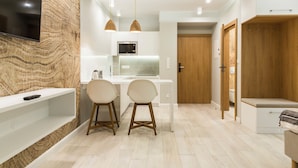 A modern kitchen with a flat-screen TV, two bar stools, a microwave, and a wooden door. - Royal Hill Residence (Zakopane)