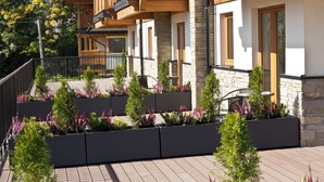 A modern building with a stone facade, wooden balconies, and a landscaped garden with various plants. - Royal Hill Residence (Zakopane)