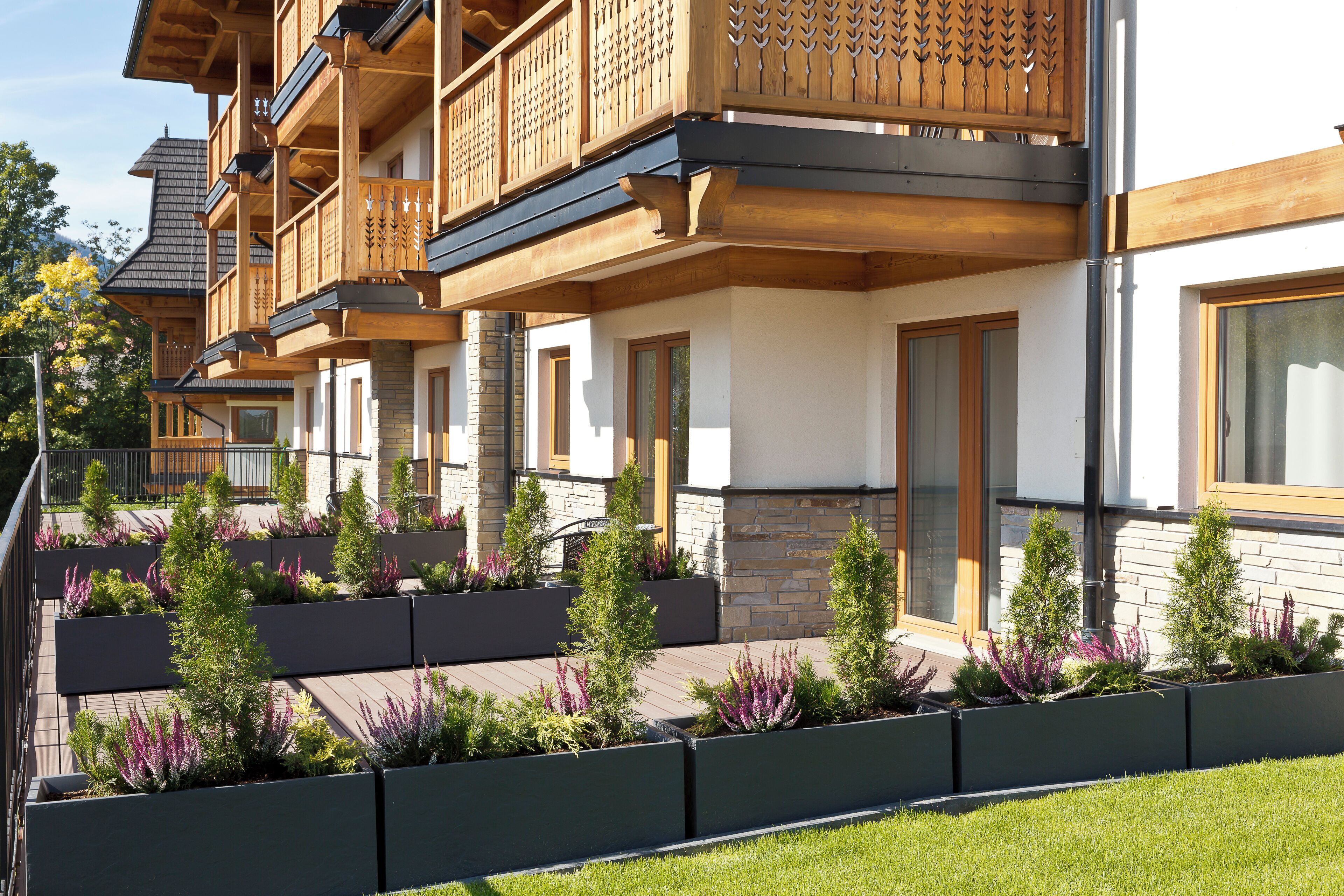 A multi-story building with wooden balconies, stone facade, and landscaped garden beds.