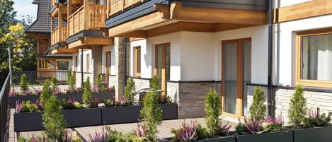 A multi-story building with wooden balconies, stone facade, and landscaped garden beds.
