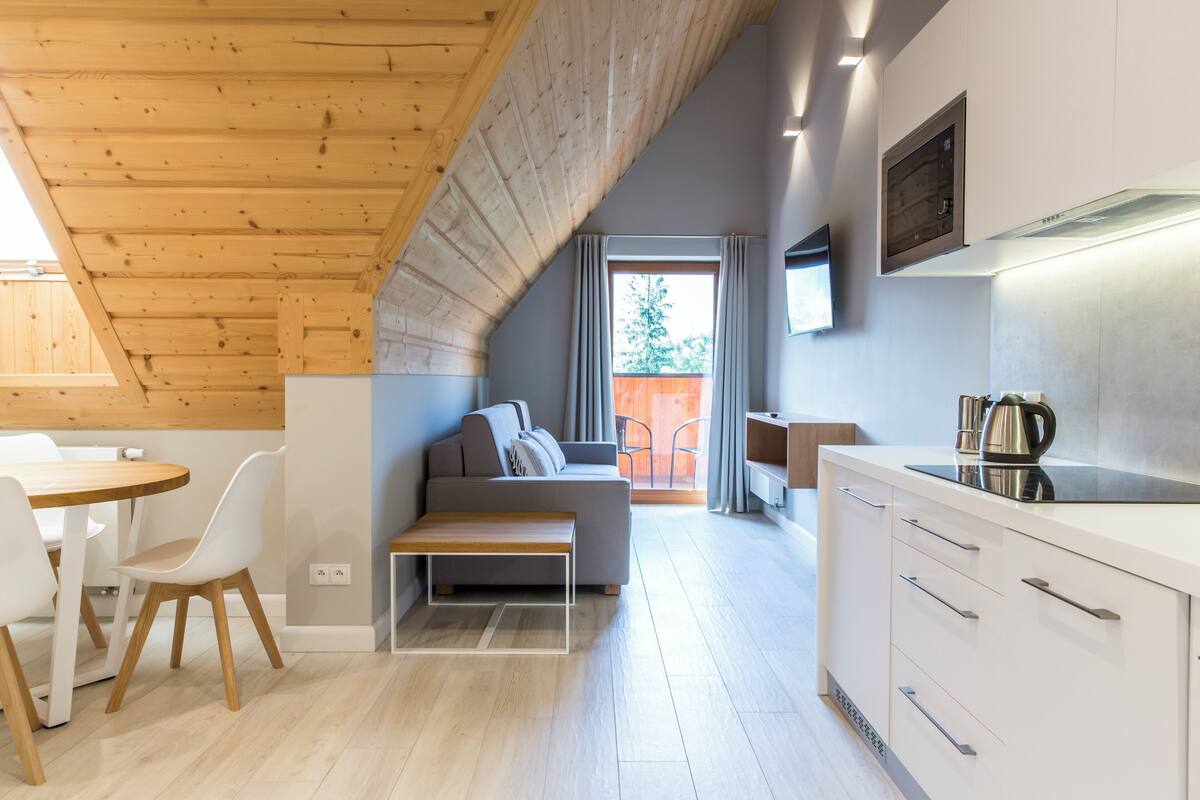 Una cucina moderna con mobili bianchi, soffitto in legno e un'area pranzo con una panca e sedie.