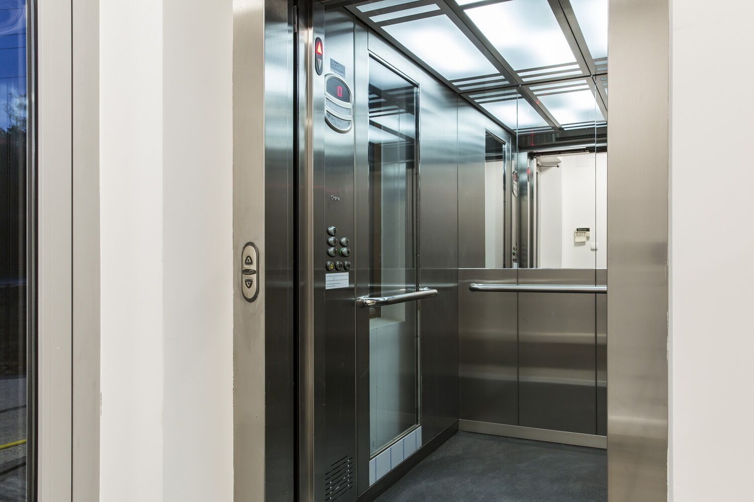A modern elevator with stainless steel doors and a control panel with emergency buttons.