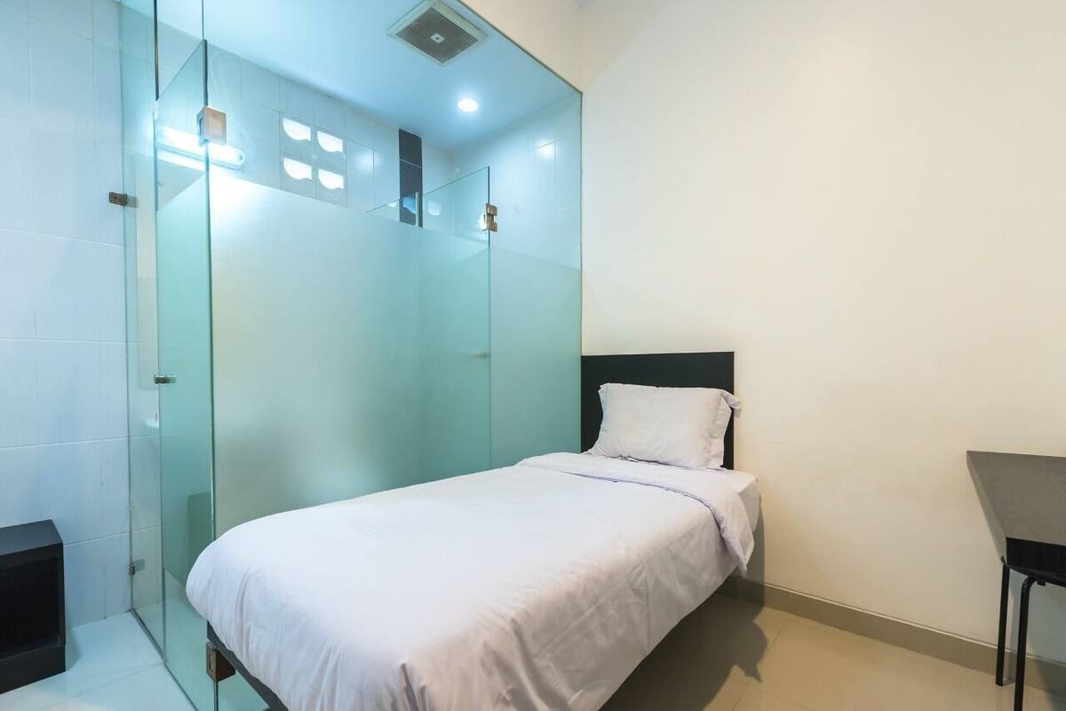 A modern bedroom with a glass shower enclosure, a bed with white bedding, and a small table.