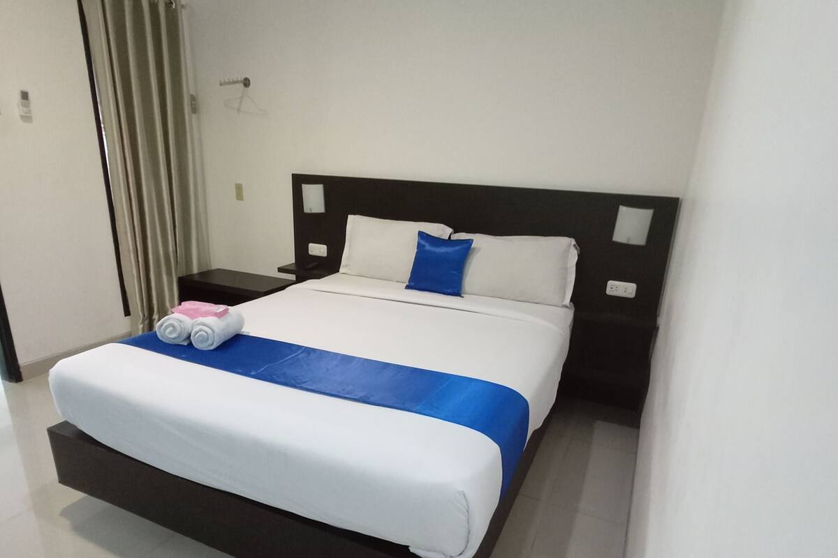 A hotel room with a large bed, a nightstand, a lamp, and a window with curtains.