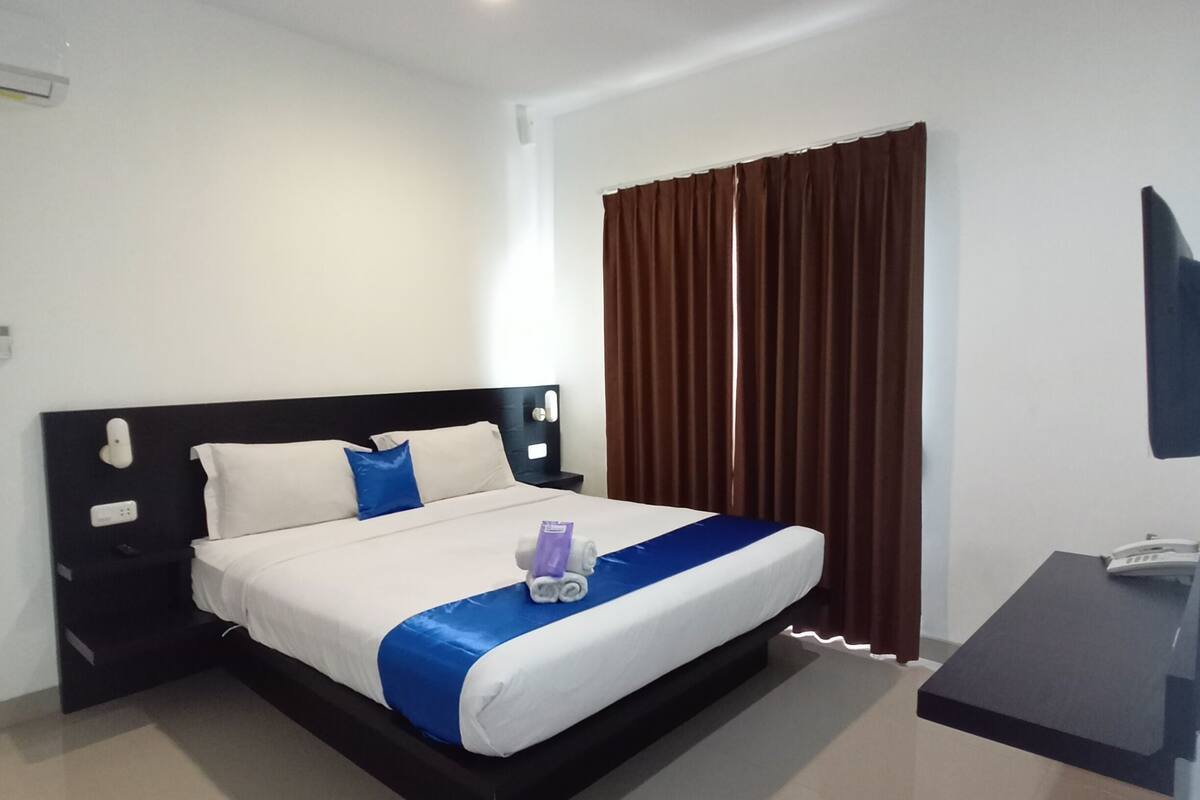 A hotel room with a bed, nightstands, a desk, and a television.