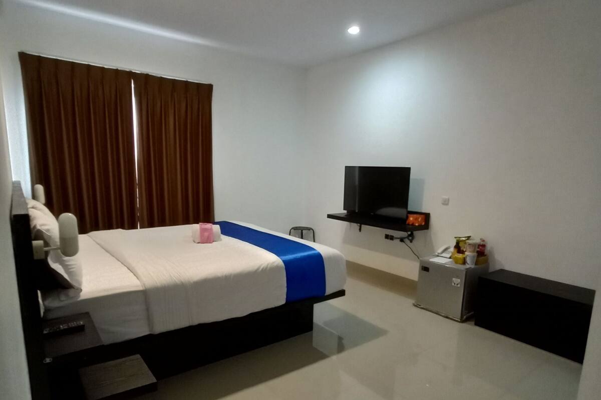 A hotel room with a bed, a television, a small table, and a heater.