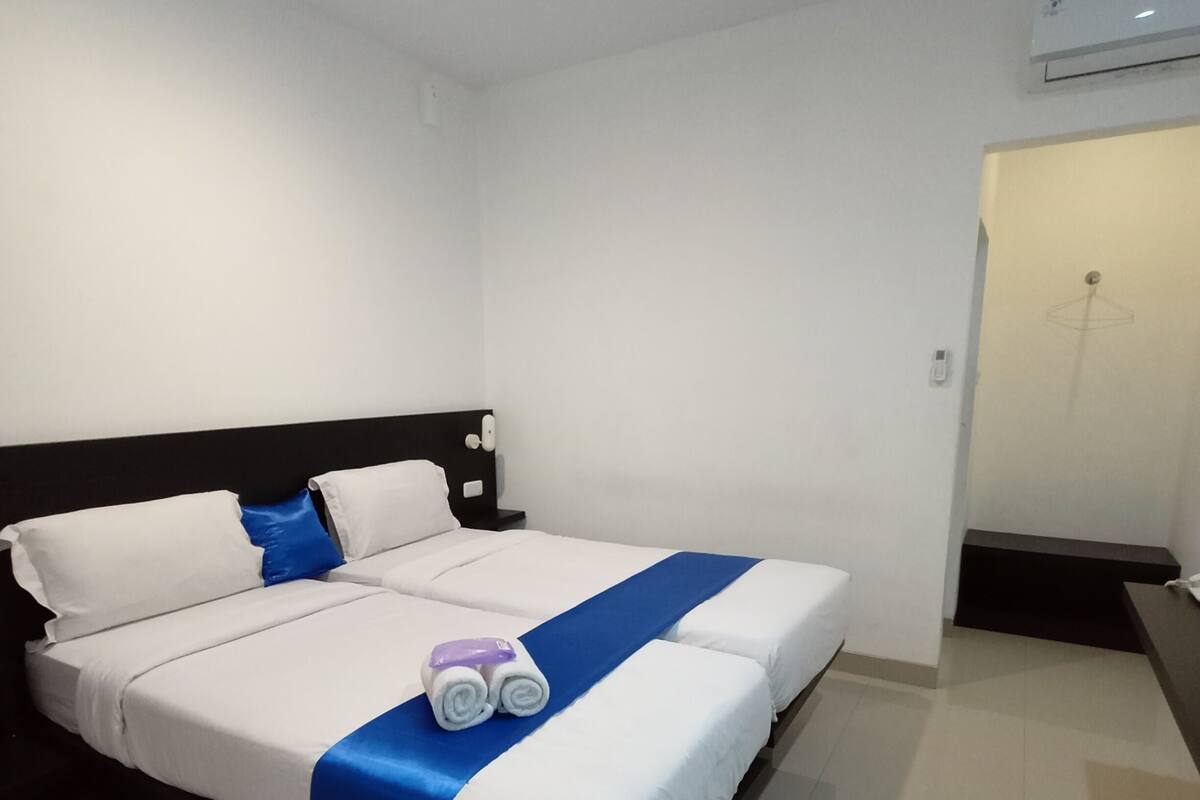 A hotel room with a bed, a bedside table, a nightstand, and an air conditioning unit on the wall.
