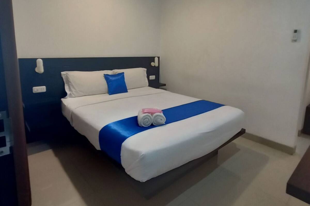 A neatly made bed with a blue accent, white bedding, and a pink towel.