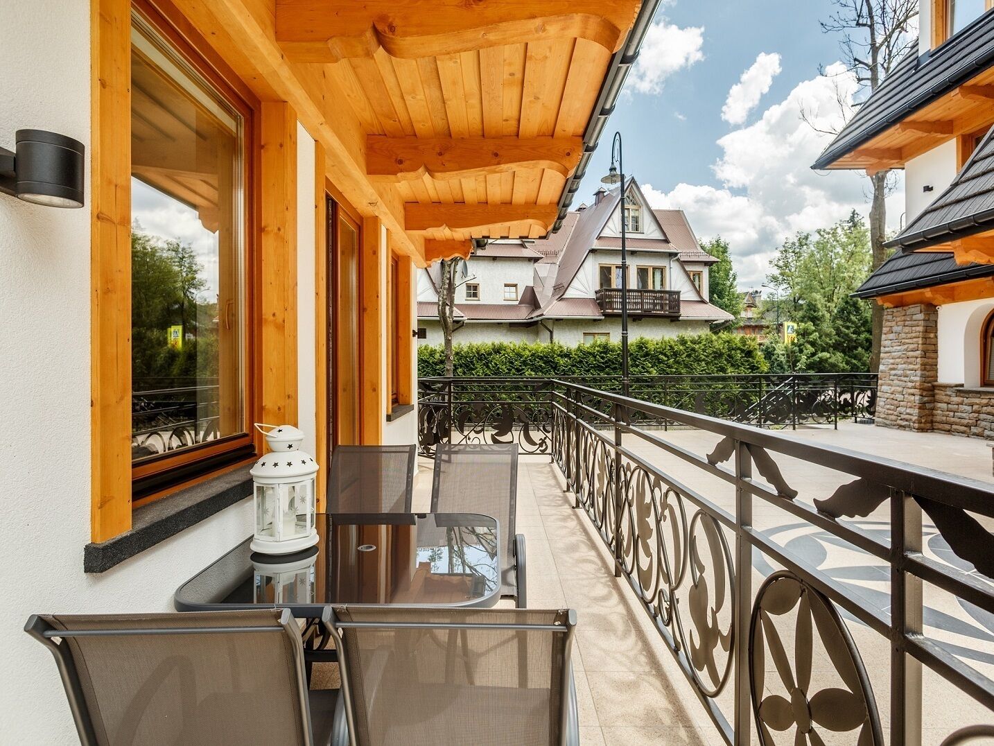 A balcony with a table and chairs, wooden beams, and a view of a house in the background.