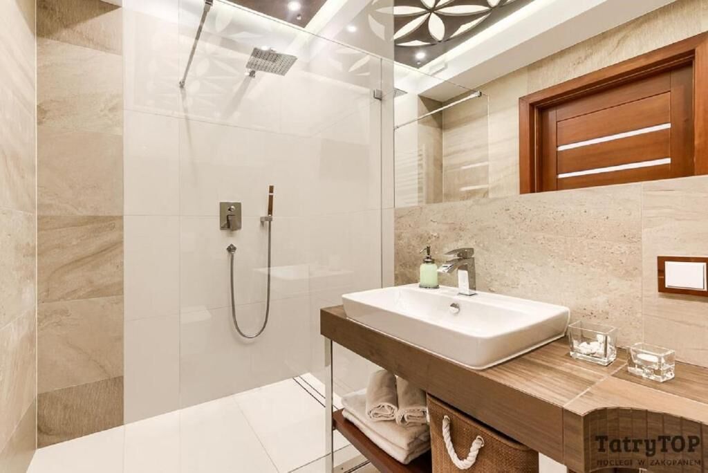 A modern bathroom with a glass-enclosed shower, a wooden vanity with a sink, and a marble-tiled floor.