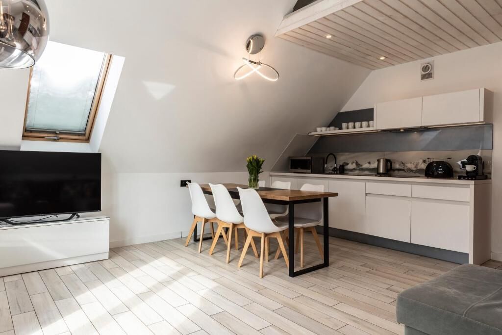 A modern kitchen with white cabinets, a dining area with a table and chairs, a TV, and a skylight.