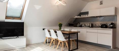A modern kitchen with white cabinets, a dining area with a table and chairs, a TV, and a skylight.