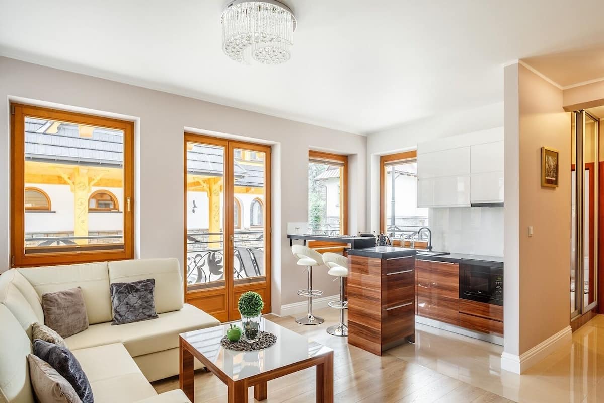 A modern apartment with a living area, kitchen, and dining space. It features large windows, a chandelier, and a balcony.