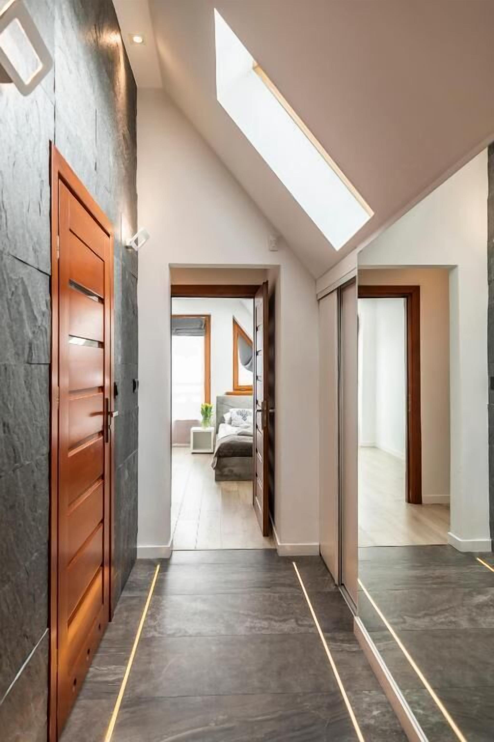 A modern hallway with a skylight, dark flooring, and wooden doors.