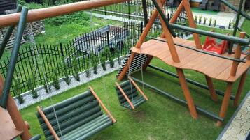 Estructura de juego de madera con tobogán y columpios, rodeada de un jardín cercado.