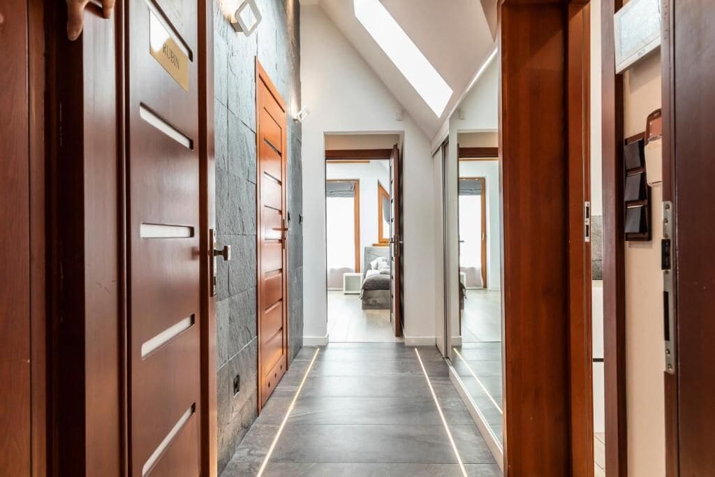 A hallway with wooden doors, a stone wall, and a skylight.