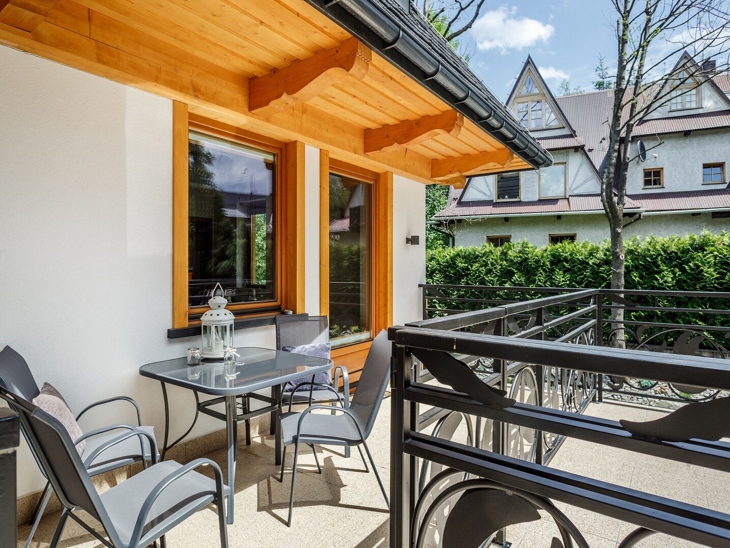Un patio al aire libre con una mesa, sillas, un farol y vistas a una casa vecina.