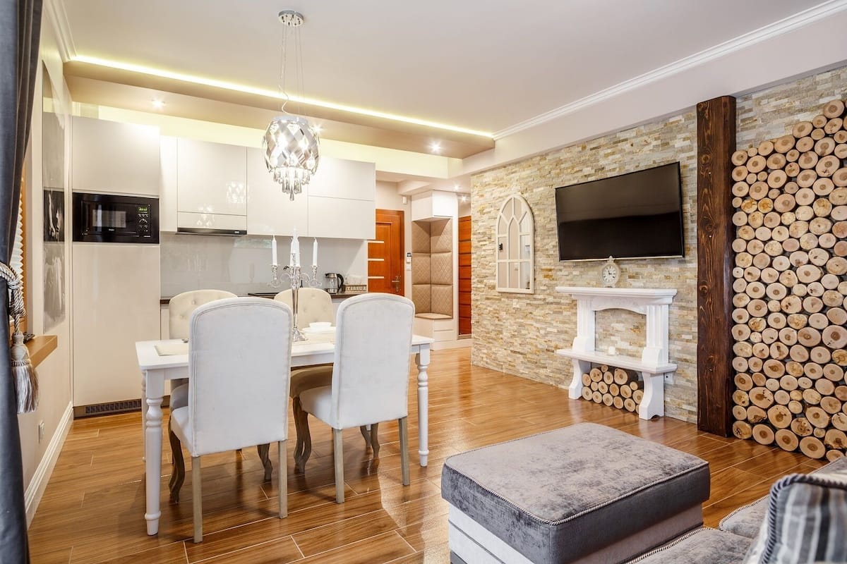 A modern kitchen with white cabinets, a chandelier, and a dining area with white chairs.
