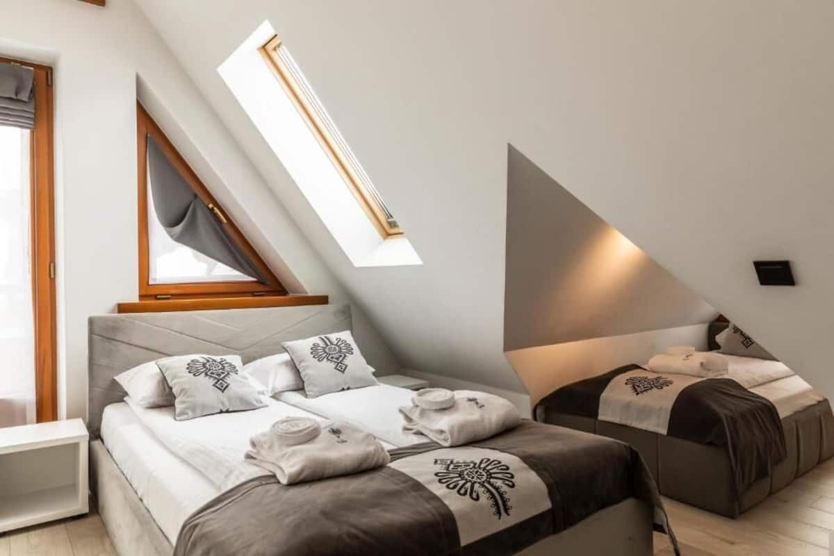 A modern bedroom with a skylight, a bed with decorative pillows, and a bedside table.