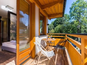 A wooden balcony with a bed, a table with chairs, and a view of trees.