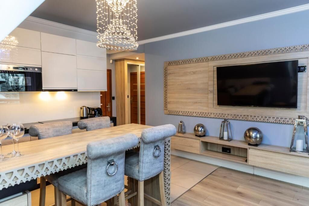 Una cocina moderna con horno empotrado, un comedor con mesa de madera y sillas acolchadas, y un televisor de pantalla plana grande montado en la pared.