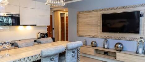 Una cocina moderna con horno empotrado, un comedor con mesa de madera y sillas acolchadas, y un televisor de pantalla plana grande montado en la pared.
