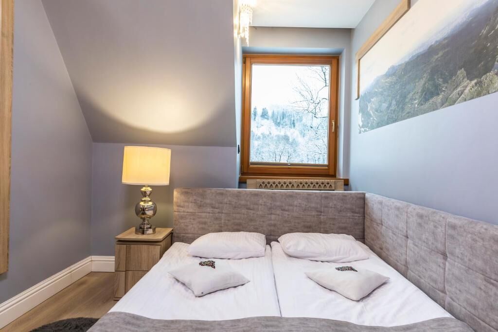 A bedroom with a bed, a nightstand, a lamp, and a window with a view of trees.