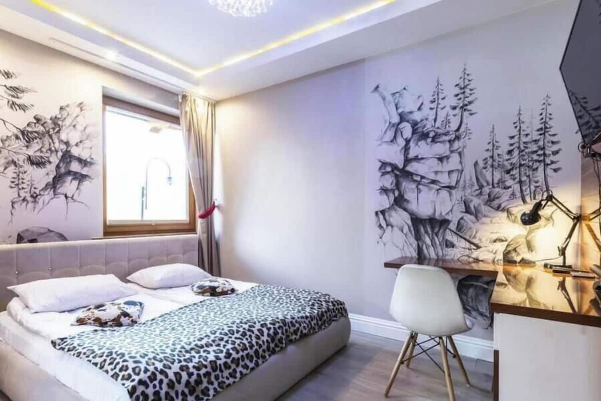 A modern bedroom with a bed, desk, and chair, featuring a large mural and a window with curtains.