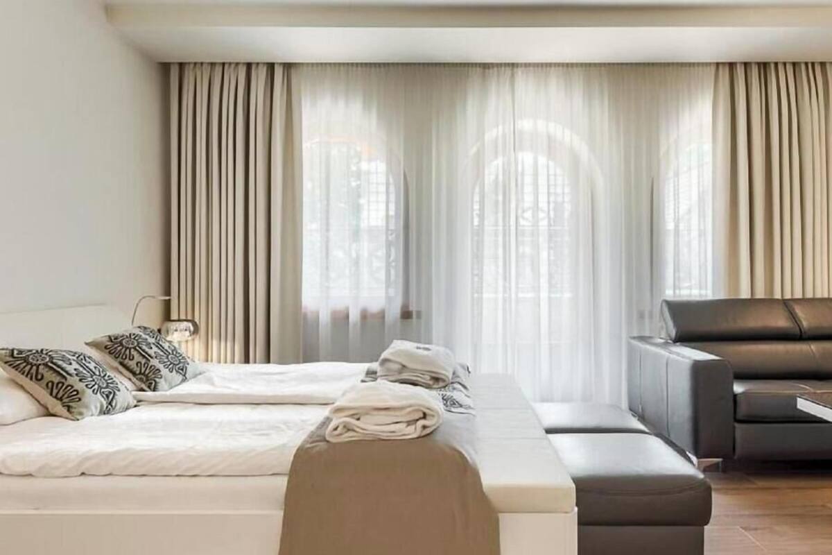 A hotel room with a bed, a sofa, a small table, and curtains.