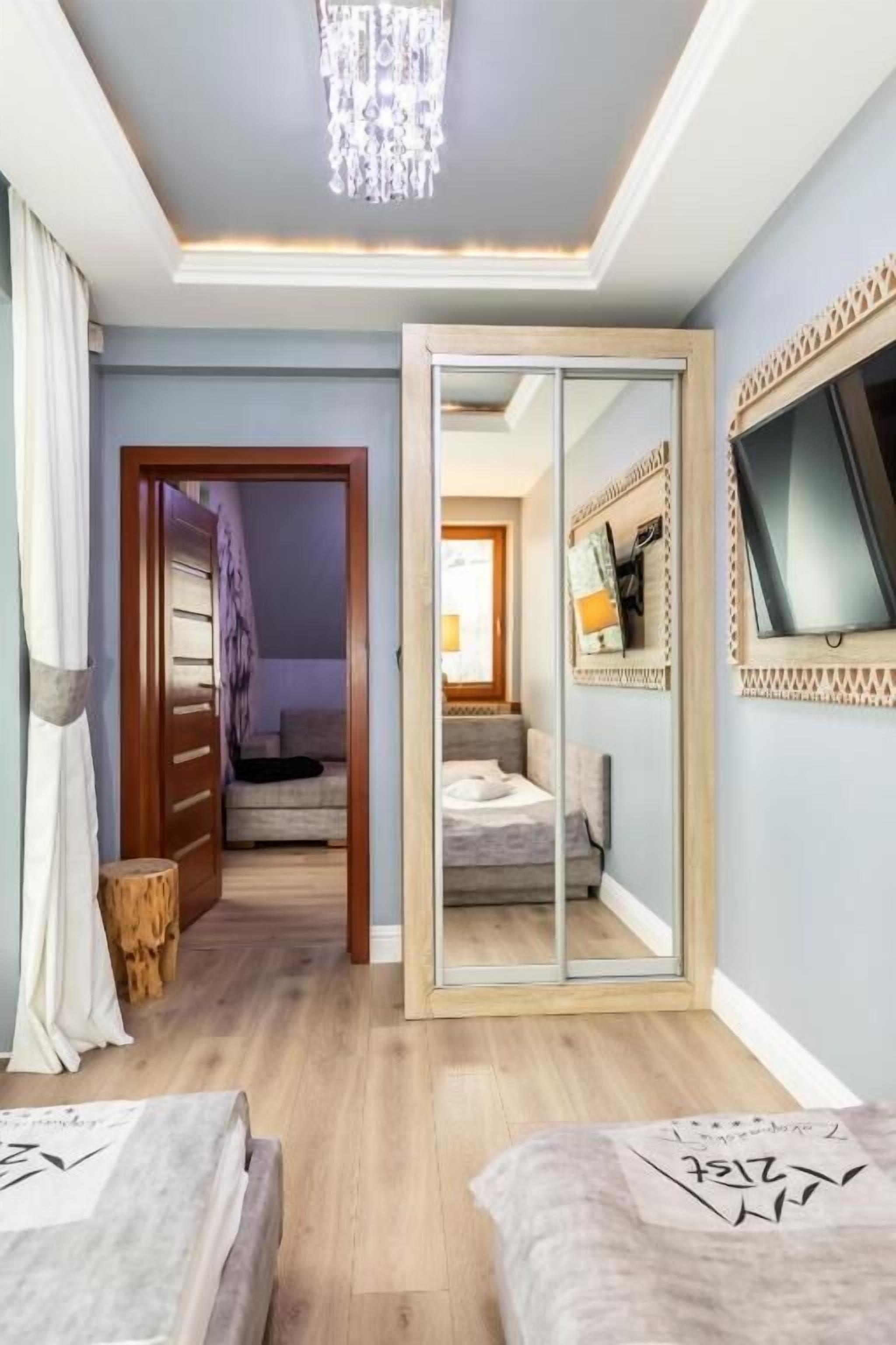 Ein Schlafzimmer mit Holzboden, einem großen Spiegel, einem Bett und einer Tür zu einem anderen Raum.