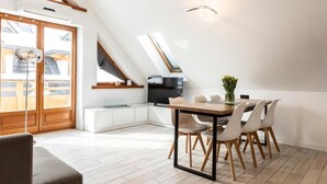 A modern loft-style room with a dining area, a TV, and a kitchenette.