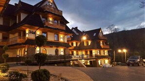 A multi-story hotel with a stone facade, multiple balconies, and a well-lit entrance.