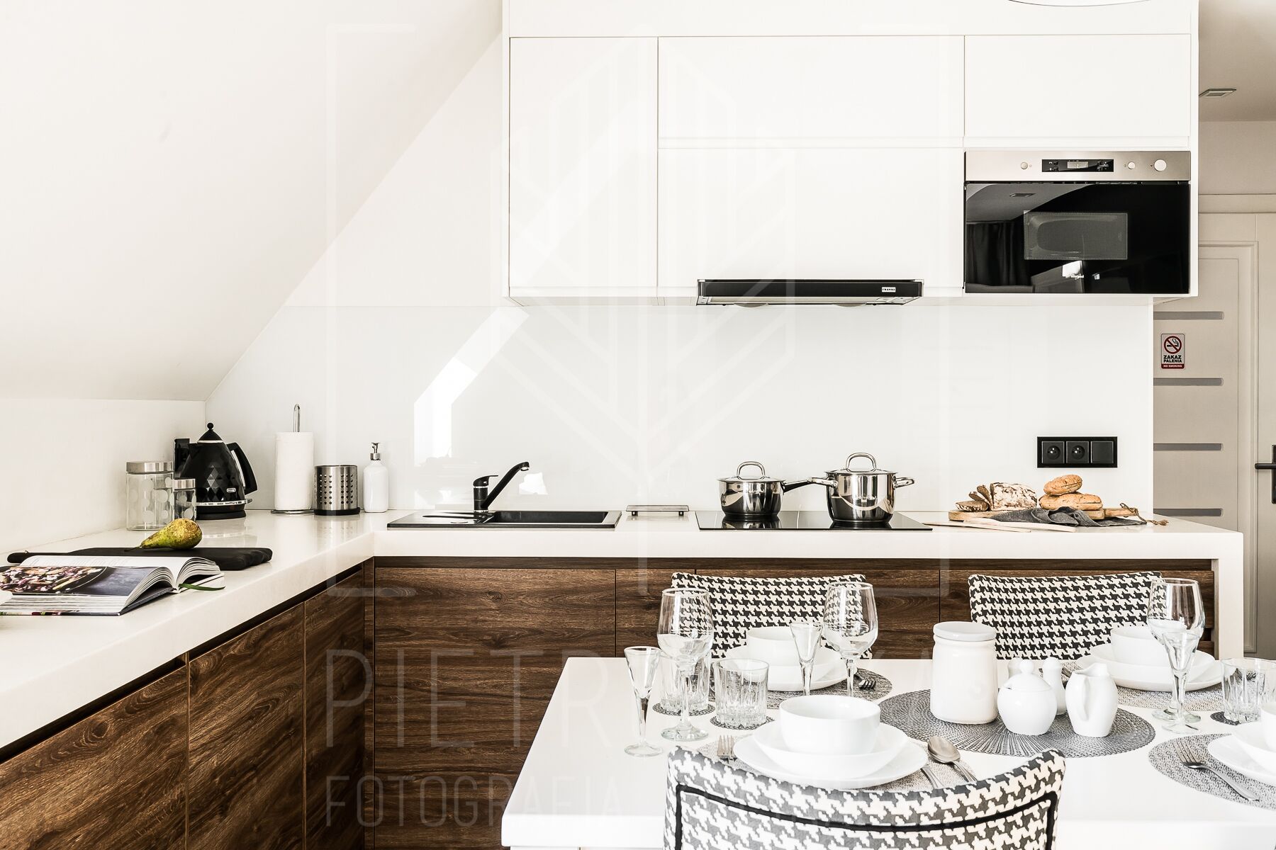 A modern kitchen with a built-in oven, a microwave, and a coffee machine. There is a dining area with a table set for four, including plates, glasses, and cutlery.