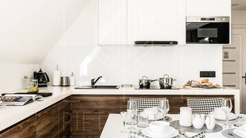 A modern kitchen with a built-in oven, a microwave, and a coffee machine. There is a dining area with a table set for four, including plates, glasses, and cutlery.