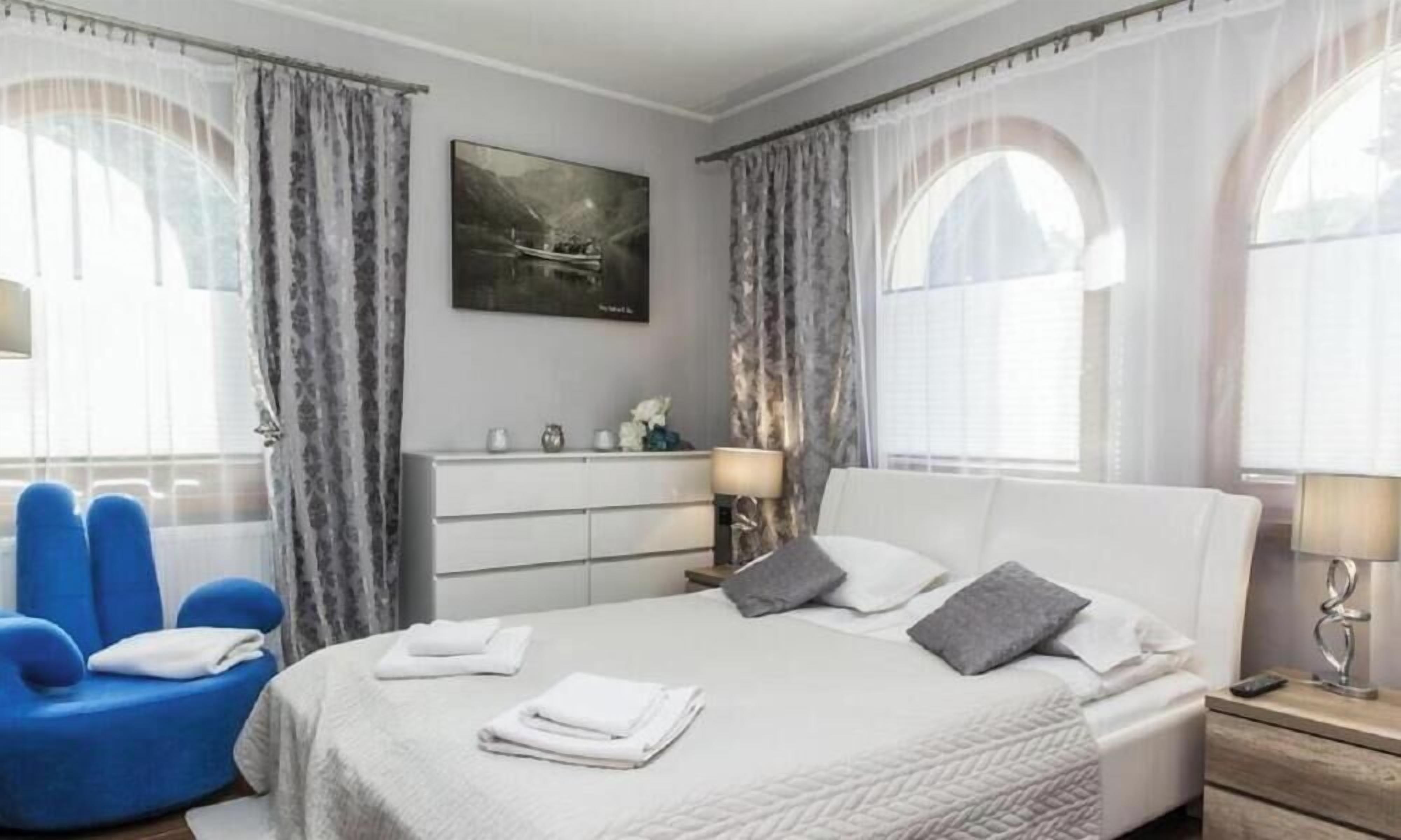 Ein Hotelzimmer mit einem Bett, einem blauen Sessel, einem Schminktisch und einem Bild an der Wand.