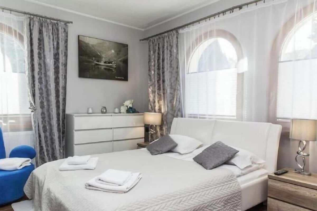 A hotel room with a bed, a blue chair, a dresser, and a painting on the wall.