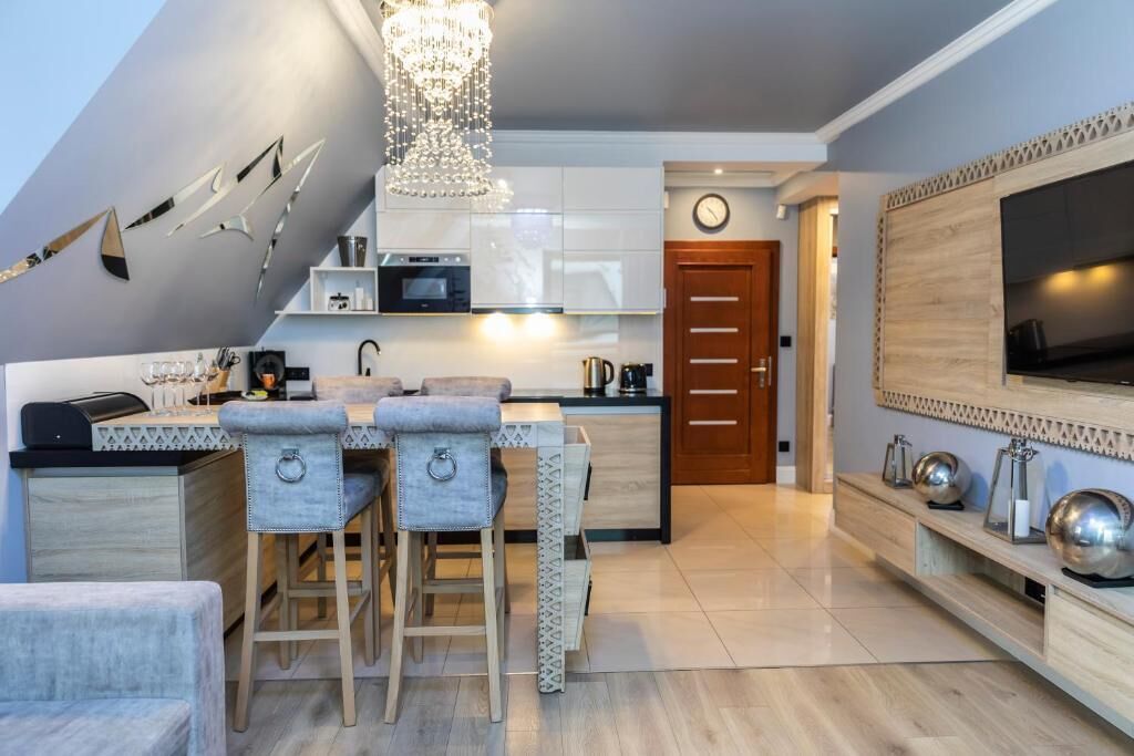 Eine moderne Küche mit weißen Schränken, einer Bar mit Hockern, einer Kristallleuchtreiter und einem an der Wand befestigten Flachbildfernseher.