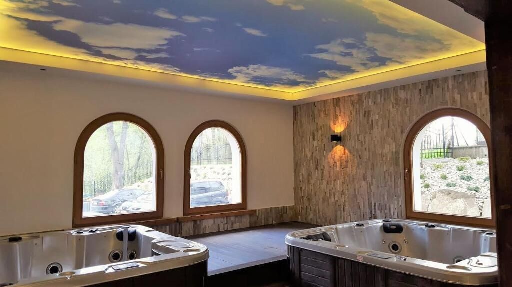 Une salle de spa dotée de deux bains à remous, d’un mur en bois et d’un plafond orné de motifs de nuages.
