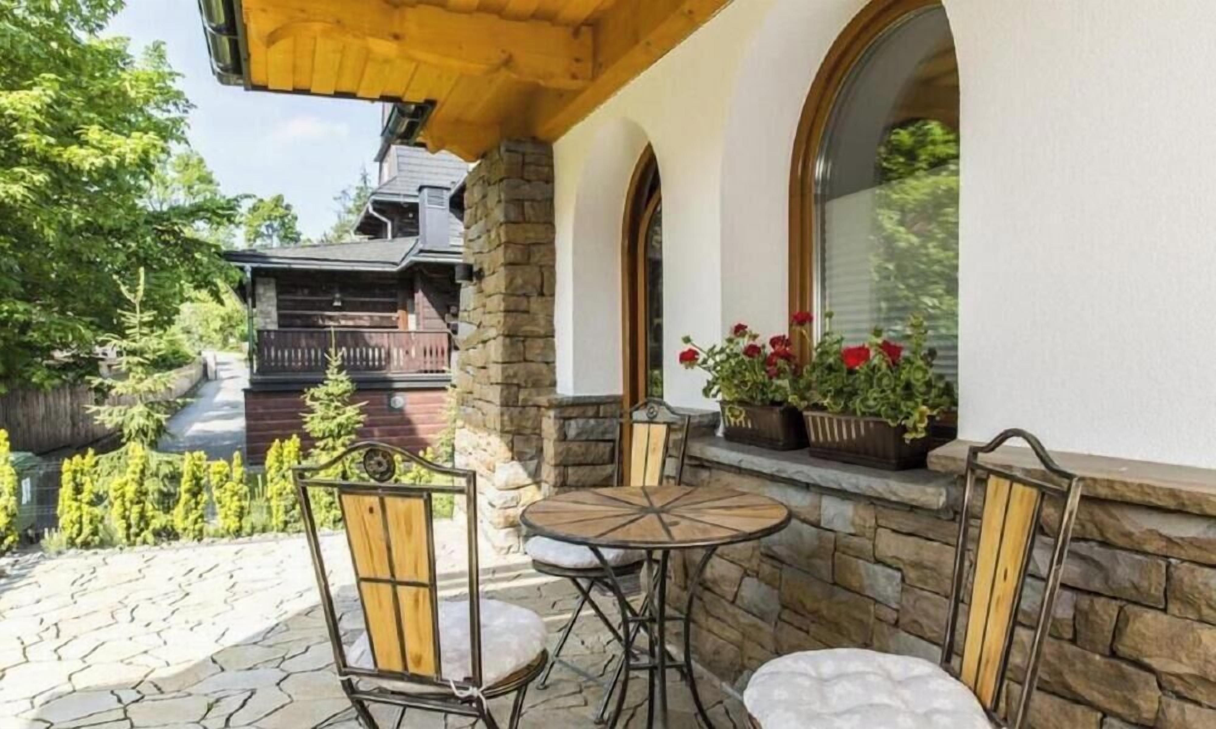 A patio with stone flooring, a wooden table, and two chairs.