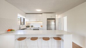 A modern kitchen with white cabinetry, a stainless steel refrigerator, and a marble countertop.