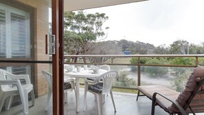 A balcony with a table set for tea, white plastic chairs, and a cushioned chair.