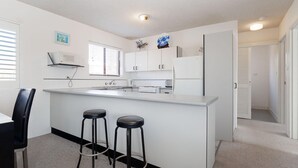 A modern kitchen with white cabinetry, a central island with stools, a microwave, and a stove.