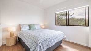 A bedroom with a bed, two bedside tables, a window with a view, and a door.