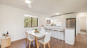 A modern kitchen with white cabinetry, a stainless steel refrigerator, and a dining area with a white table and chairs.