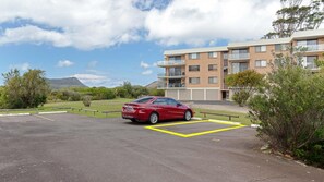 Une voiture rouge est garée dans un immeuble à plusieurs étages, devant lequel se trouve un parking.