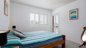 A bedroom with a bed, a bedside lamp, a window with blinds, and a framed picture on the wall.